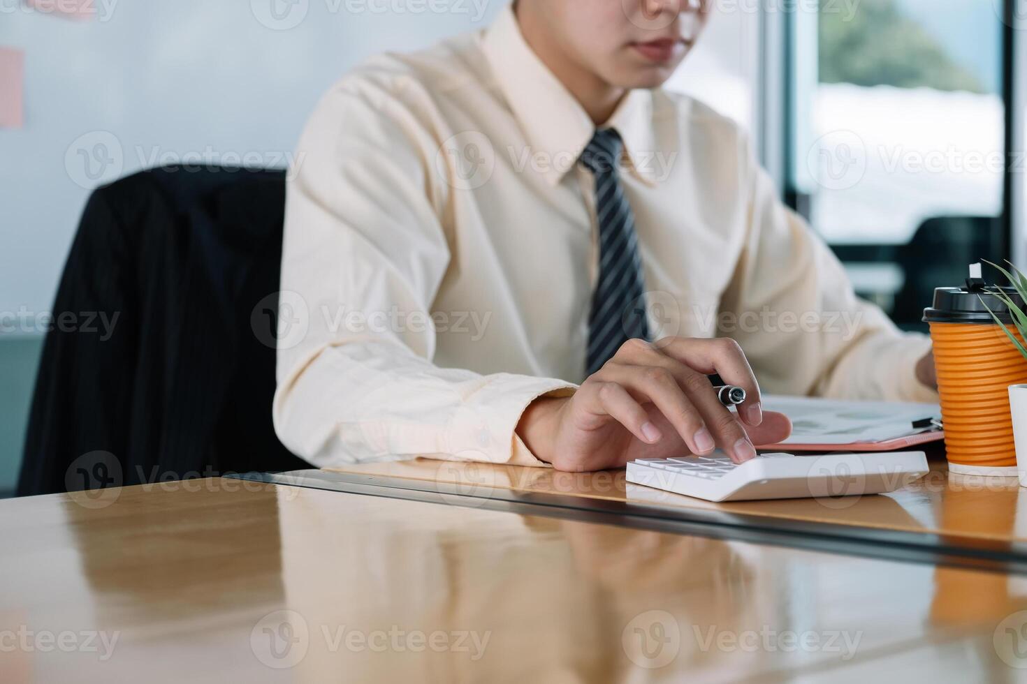 Close up of businessman or accountant hand holding pen working on calculator to calculate business data, accountancy document and laptop computer at office, business concept photo