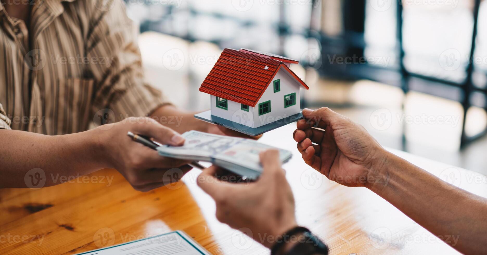 Close up of hands giving house model to other hands with money. Concept of real estate and deal. photo