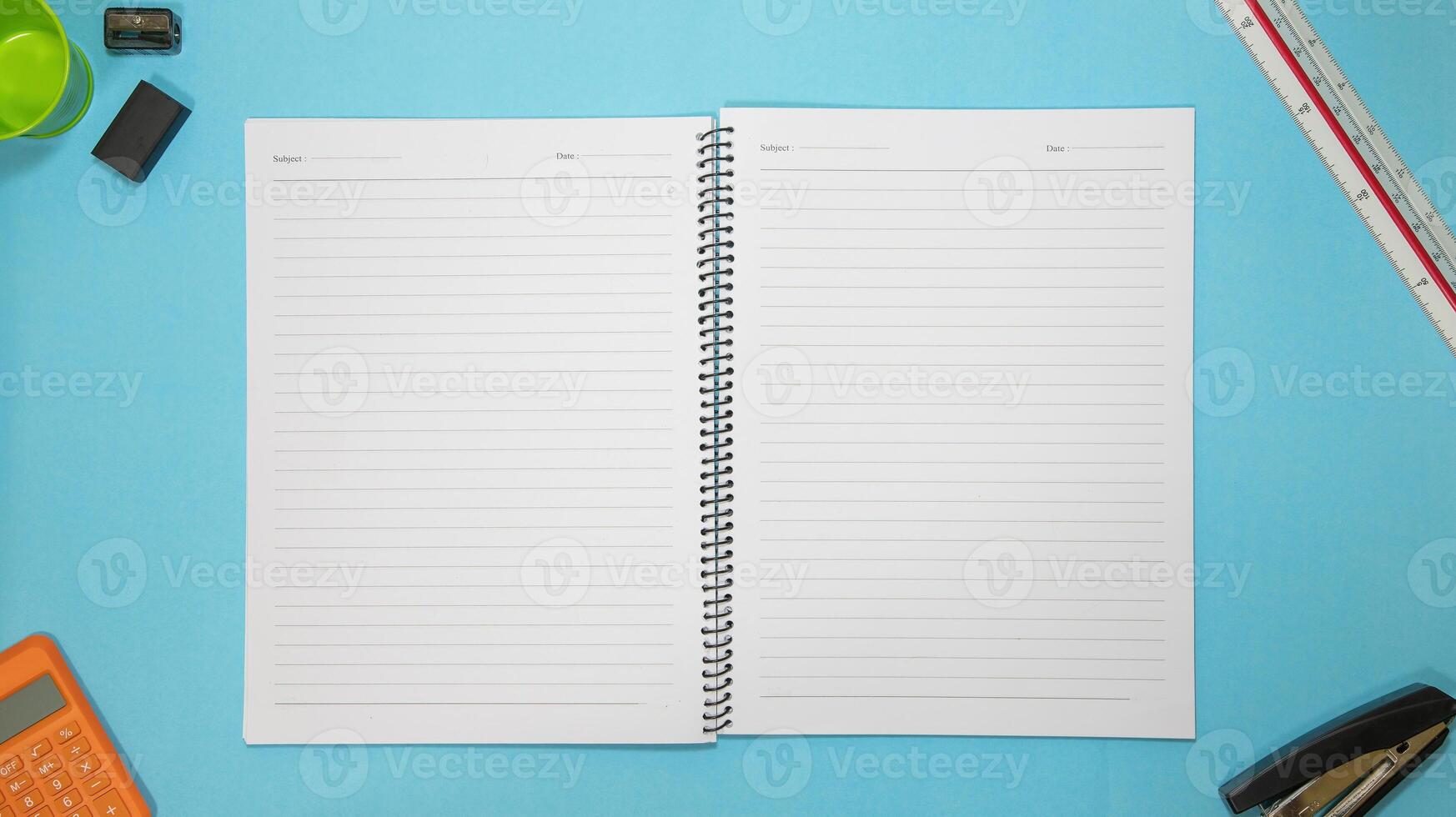 Office table desk with set of colorful supplies, blue blank note pad, cup, pen, pc, crumpled paper, flower on blue background. Top view and copy space for text. photo