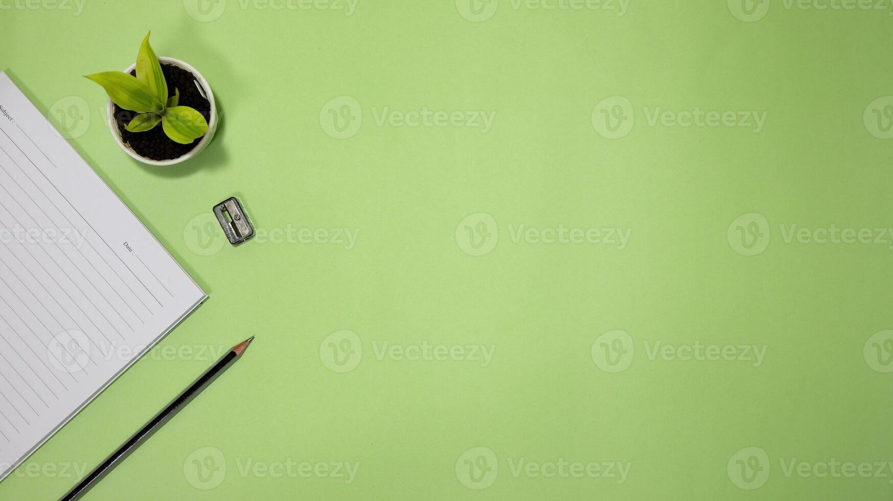 Flat lay black to school and education concept on green background with blank notepad, pencil, green plant and supplies photo