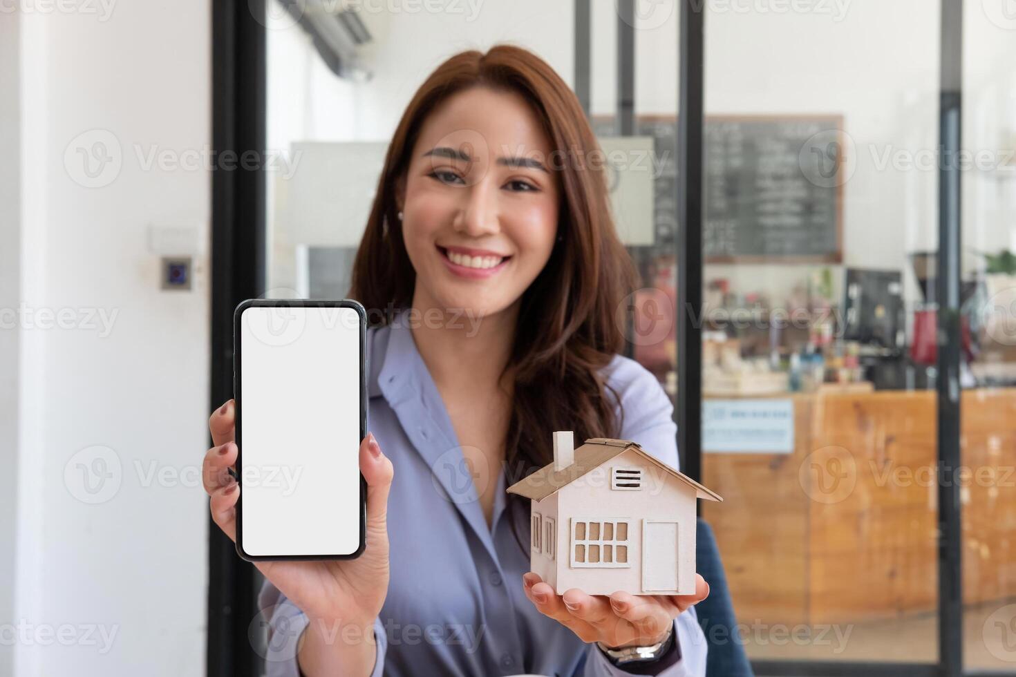 Real estate agent showing house model and mobile phone with blank white screen for advertisement photo
