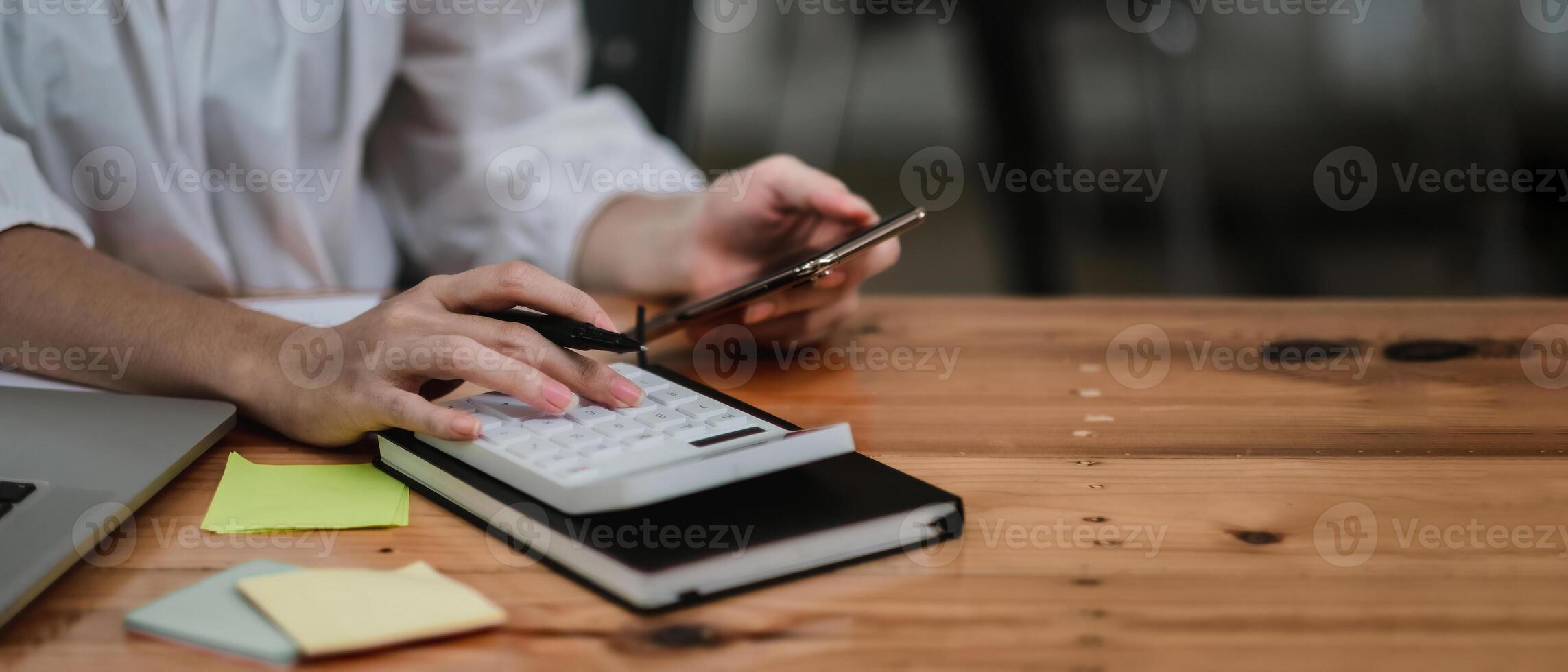 Close up hand of accounant or bookkeeper using calculator and mobile phone, calculating financial expense at home office photo