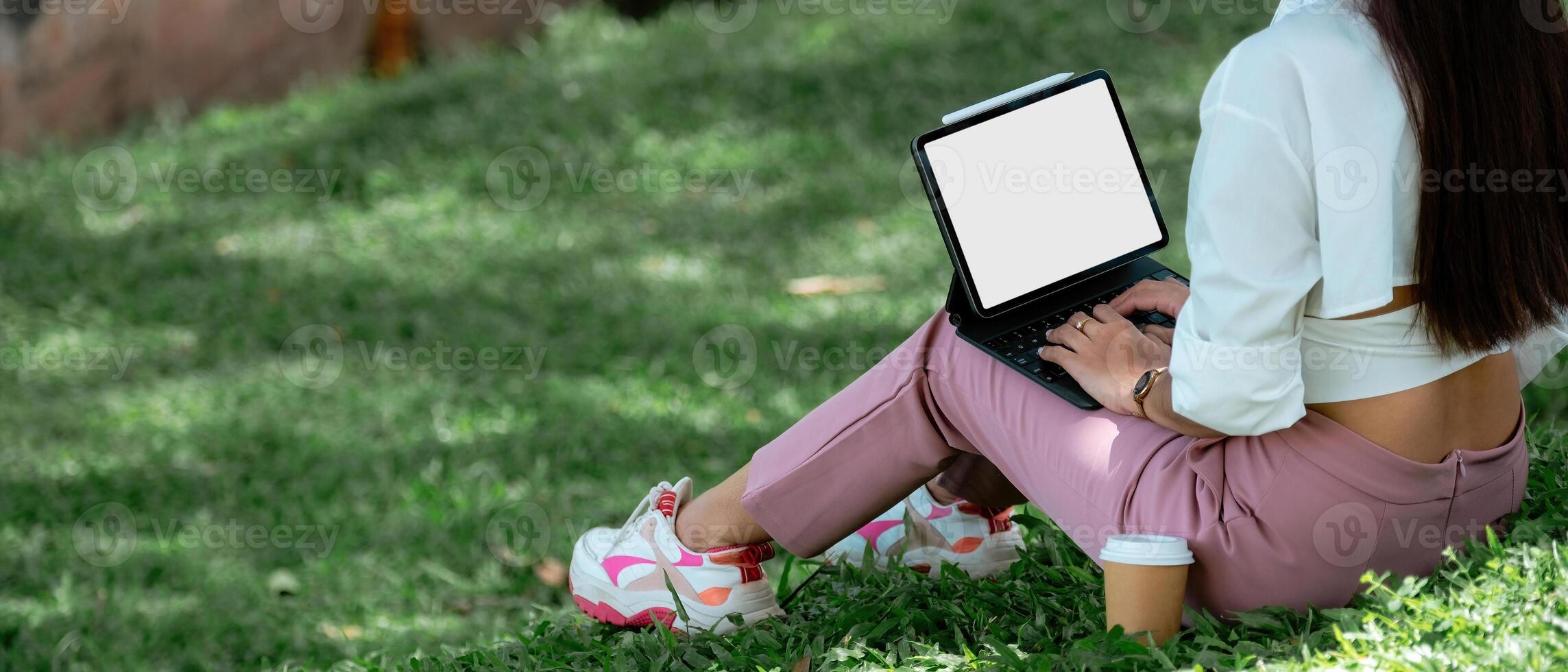 Close up student with digital tablet blank screen sitting on green grass lawn writing in notebook, technology in education, college, high school, teens concept. photo