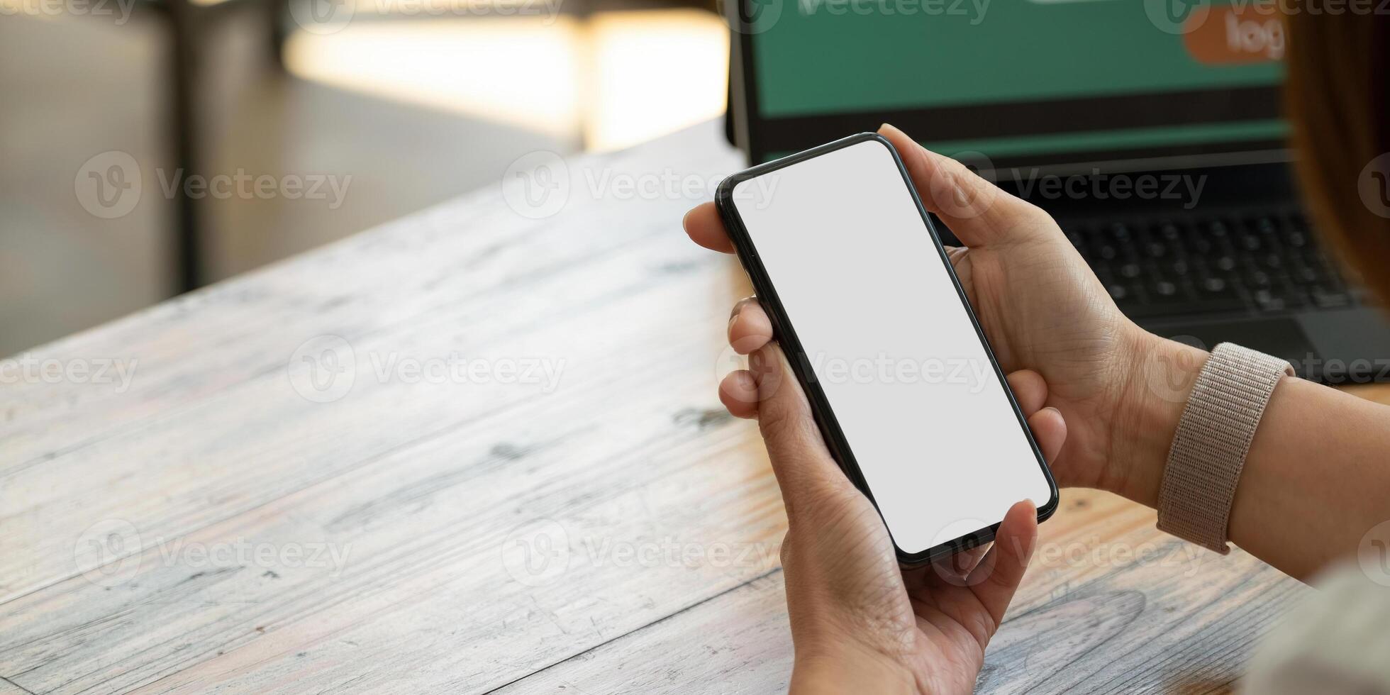 Close up hands using blank screen mobile smart phone with notebook and laptop. photo