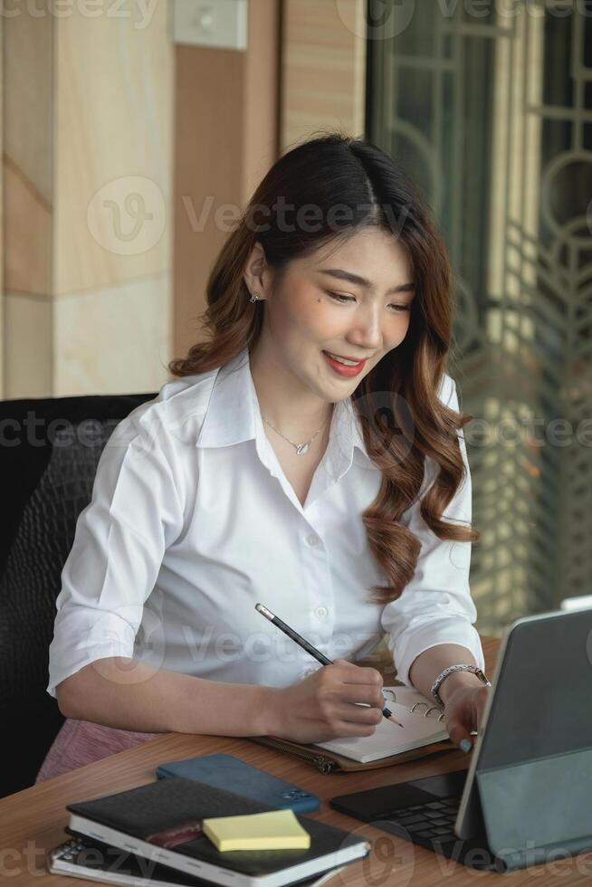 Portrait charming asian woman taking note on notepad while conference via digital tablet photo