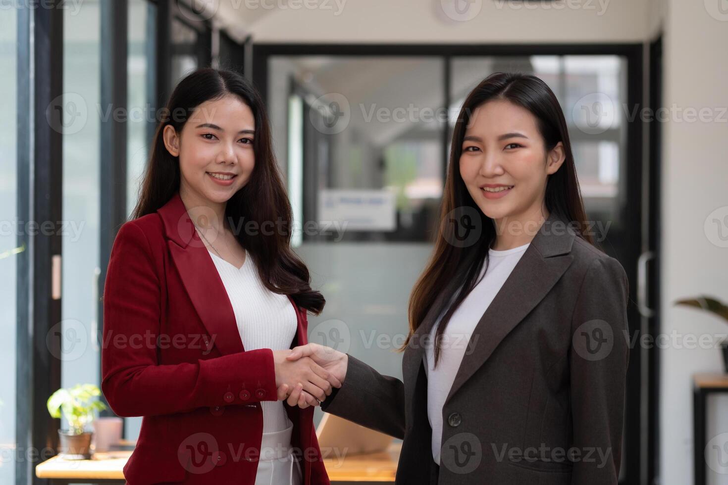 Two confident business asian woman shaking hands during looking at camera in the office, success, dealing, greeting and partner concept photo