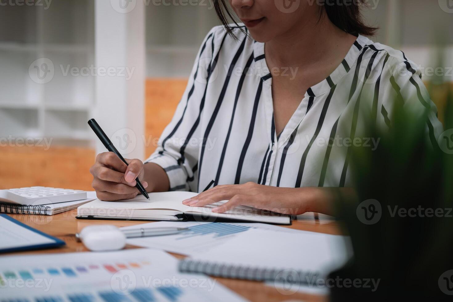 Close up of businessman or accountant hand holding pen working on calculator and laptop computer to calculate business data during make note at notepad, accountancy document at offic photo