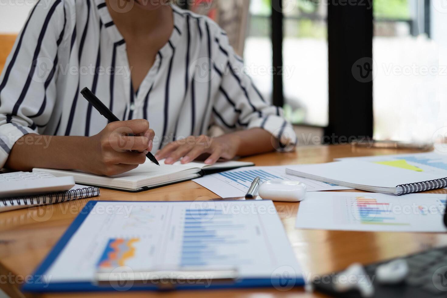 Close up of businessman or accountant hand holding pen working on calculator and laptop computer to calculate business data during make note at notepad, accountancy document at offic photo