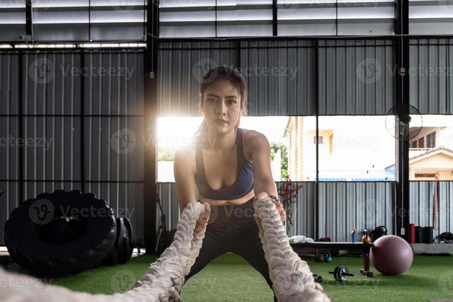 Attractive strong asian fitness woman doing battle ropes exercise at gym. weight training exercise session photo