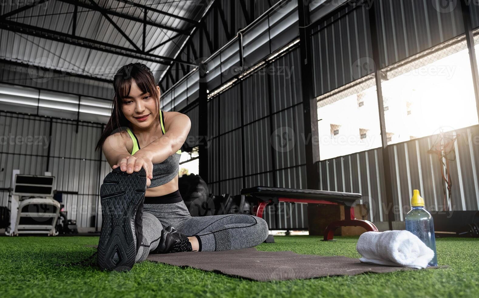 Young asian female in stylish and comfy sportswear stretching her legs on the fitness floor. exercise and sport concept. Fit woman doing stretching workout at gym photo