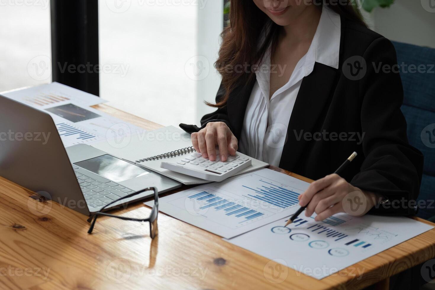Close up of businesswoman or accountant hand holding pen working on calculator to calculate business data, accountancy document and laptop computer at office, business concept. photo