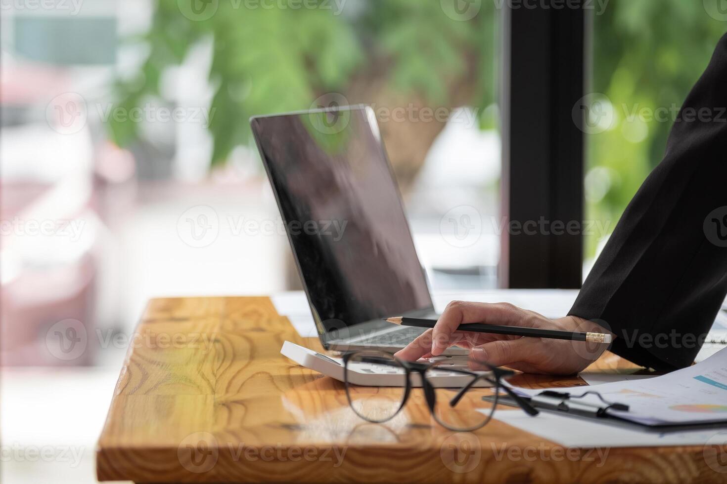Close up of business woman or accountant hand holding pen working on calculator to calculate business data, accountancy document and laptop computer at office, business concept. photo