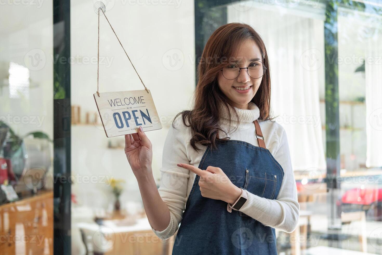 Portrait asian woman smiling and looking to camera in coffee shop. Barista female holding open sign in hand. Working woman small business owner or sme concept photo