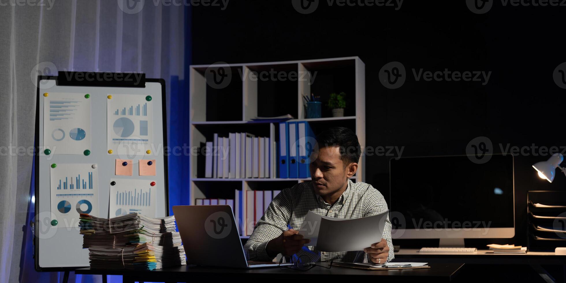 Portrait of exhausted stressed businessman work on laptop at night in dark office photo