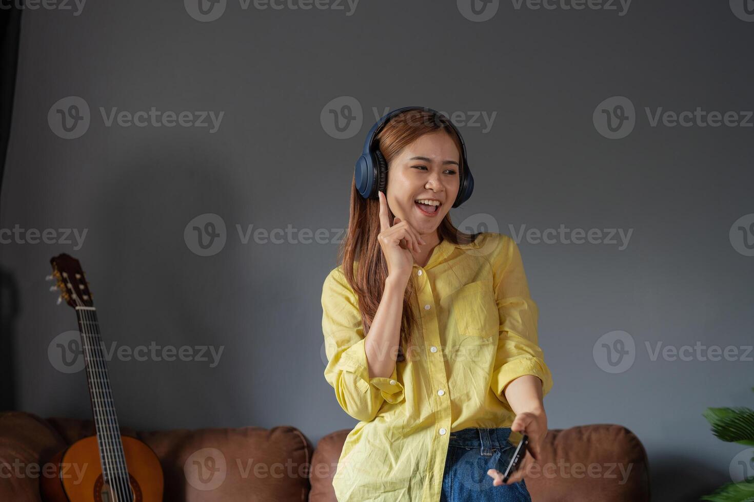 Happy woman listening music through wireless headphones standing on sofa at home. photo
