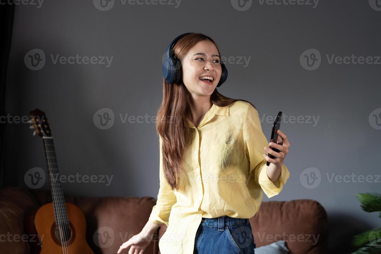 Happy woman listening music through wireless headphones standing on sofa at home. photo