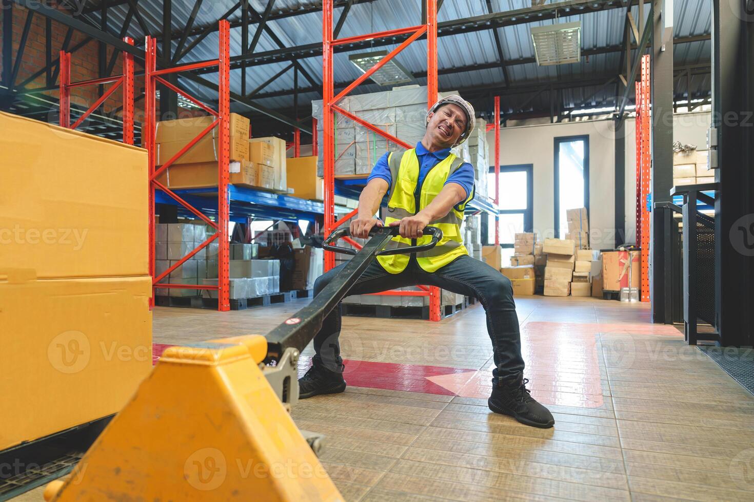 Asian male warehouse worker pulling a pallet truck. Worker working with hand pallet truck unloading cargo boxes on pallet at the warehouse. photo