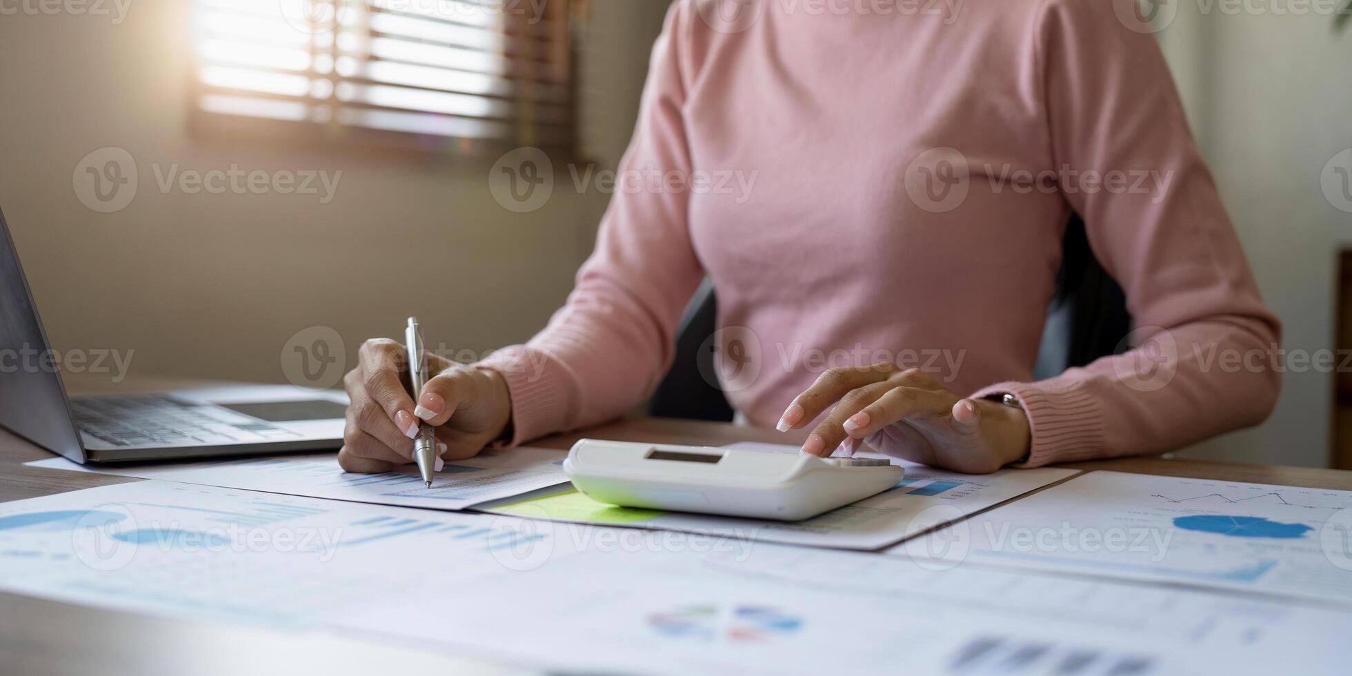 Close up of businesswoman or accountant hand holding pen working on calculator to calculate business data, accountancy document and laptop computer at office, business concept photo