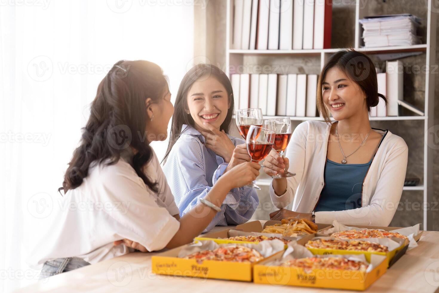 Group of Asian friends gather to celebrate Christmas with champagne and eating pizza at home. Joy of holiday party with friends or colleague concept. photo