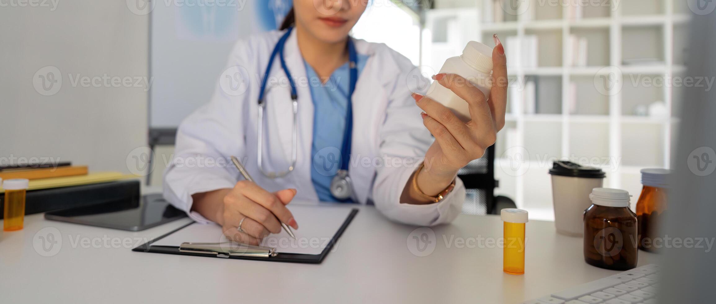 Female doctor writing in a notebook and holding a medicine bottle works at a computer while there were many medicine bottles on the table while sitting at a work desk photo