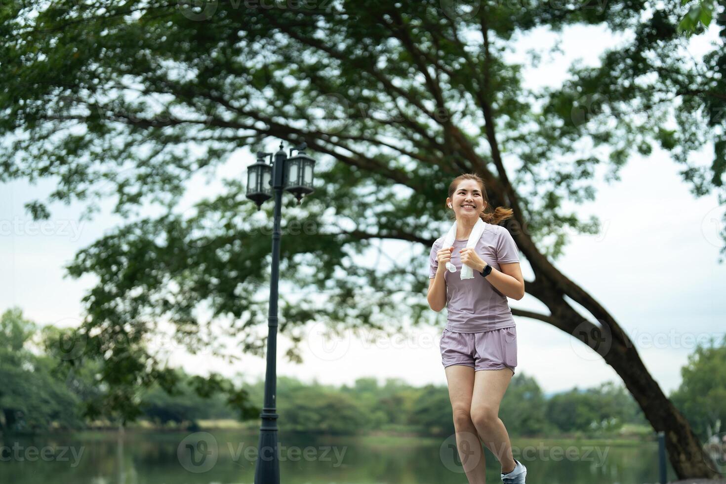 Jogging woman running in park on beautiful day off. Sport fitness model of asian ethnicity training outdoor for marathon photo