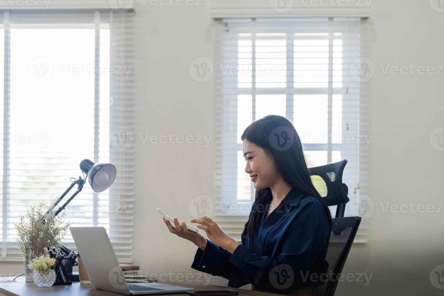 Young asian businesswoman using a calculator to calculate business principle. Accounting statistics concept at the office photo