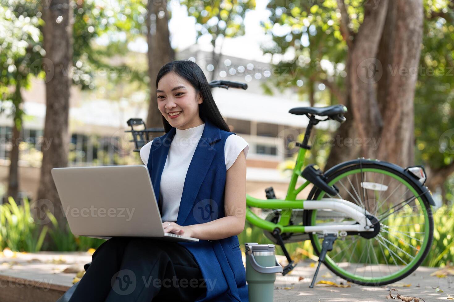 Asian businesswoman with bicycle using laptop and sitting outside the office building. Woman commuting on bike go to work. Eco friendly vehicle, sustainable lifestyle concept photo