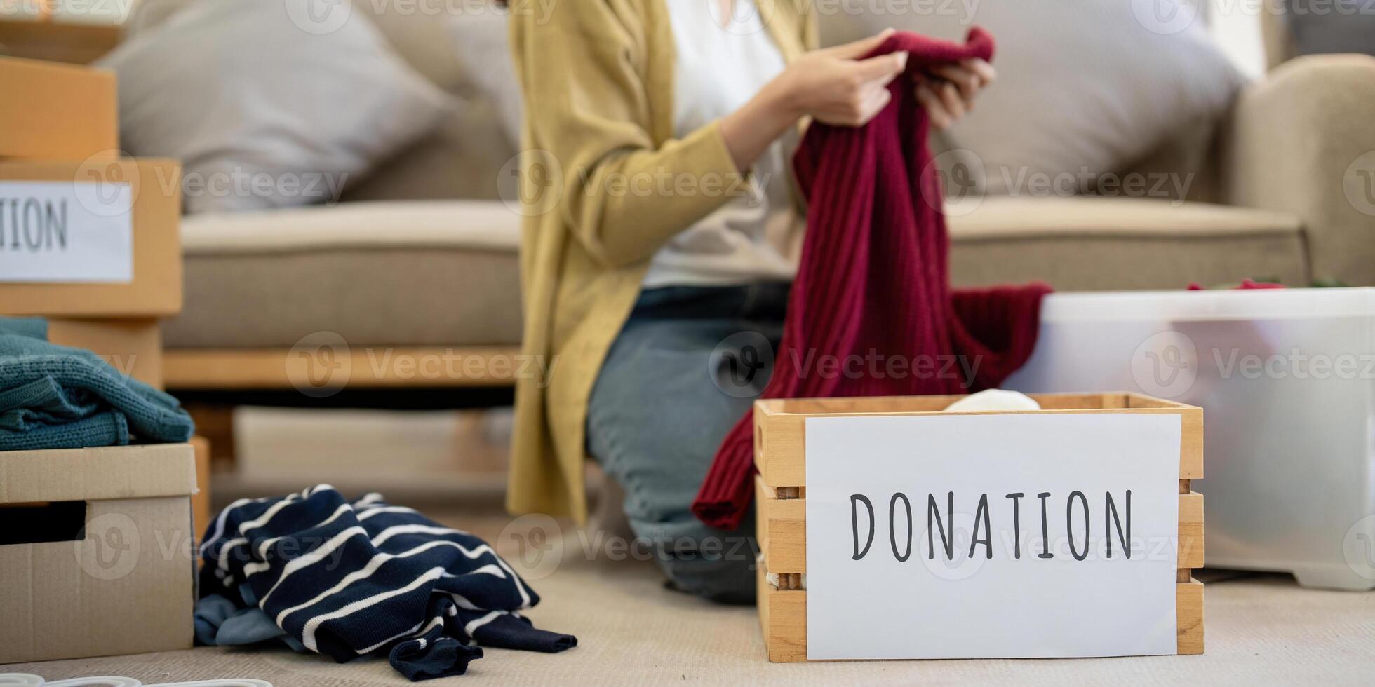 Donation, asian young woman sitting pack object at home, putting on stuff into donate box with second hand clothes, charity helping and needy people. Reuse recycle photo