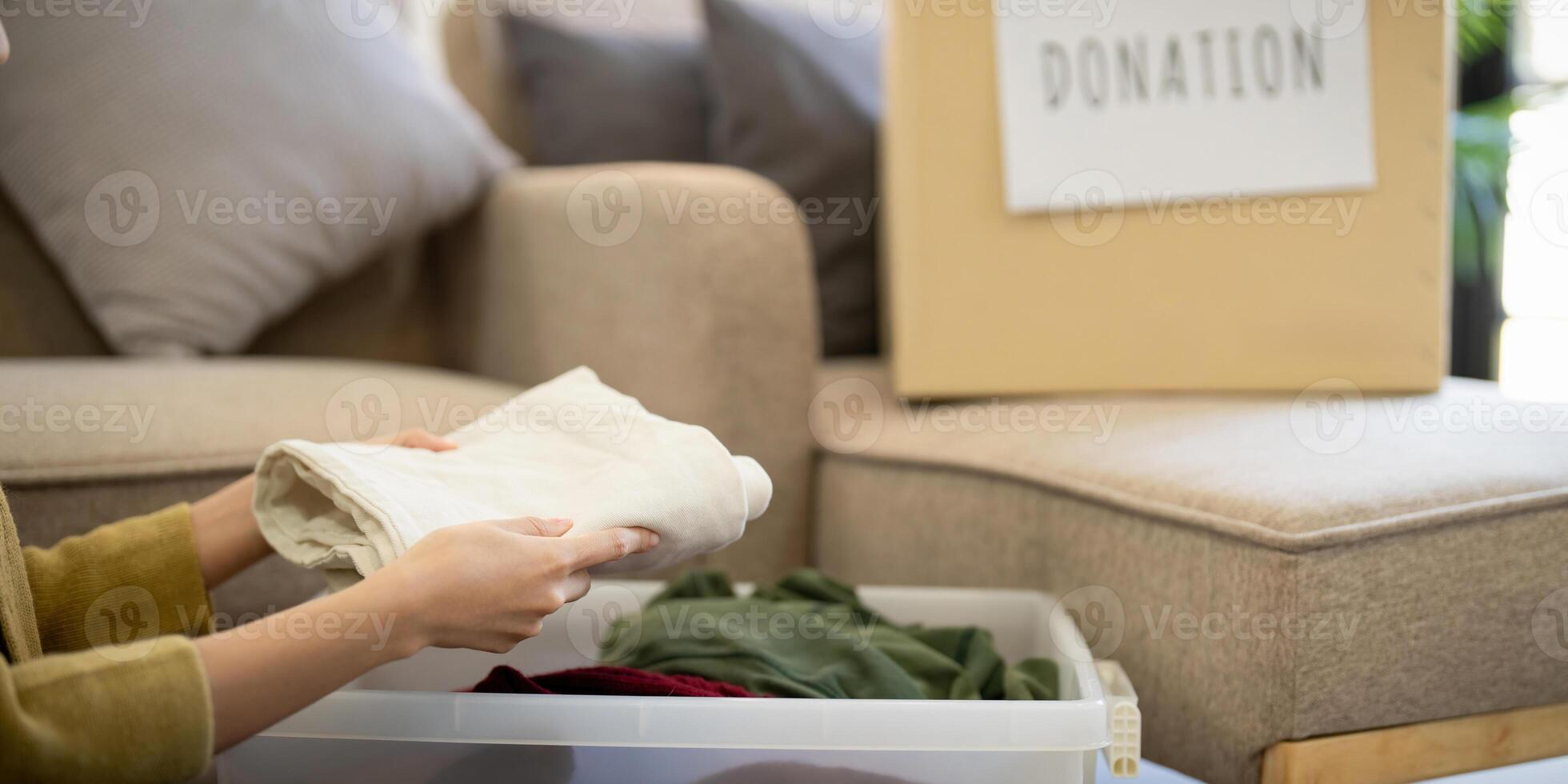 Donation, asian young woman sitting pack object at home, putting on stuff into donate box with second hand clothes, charity helping and needy people. Reuse recycle photo