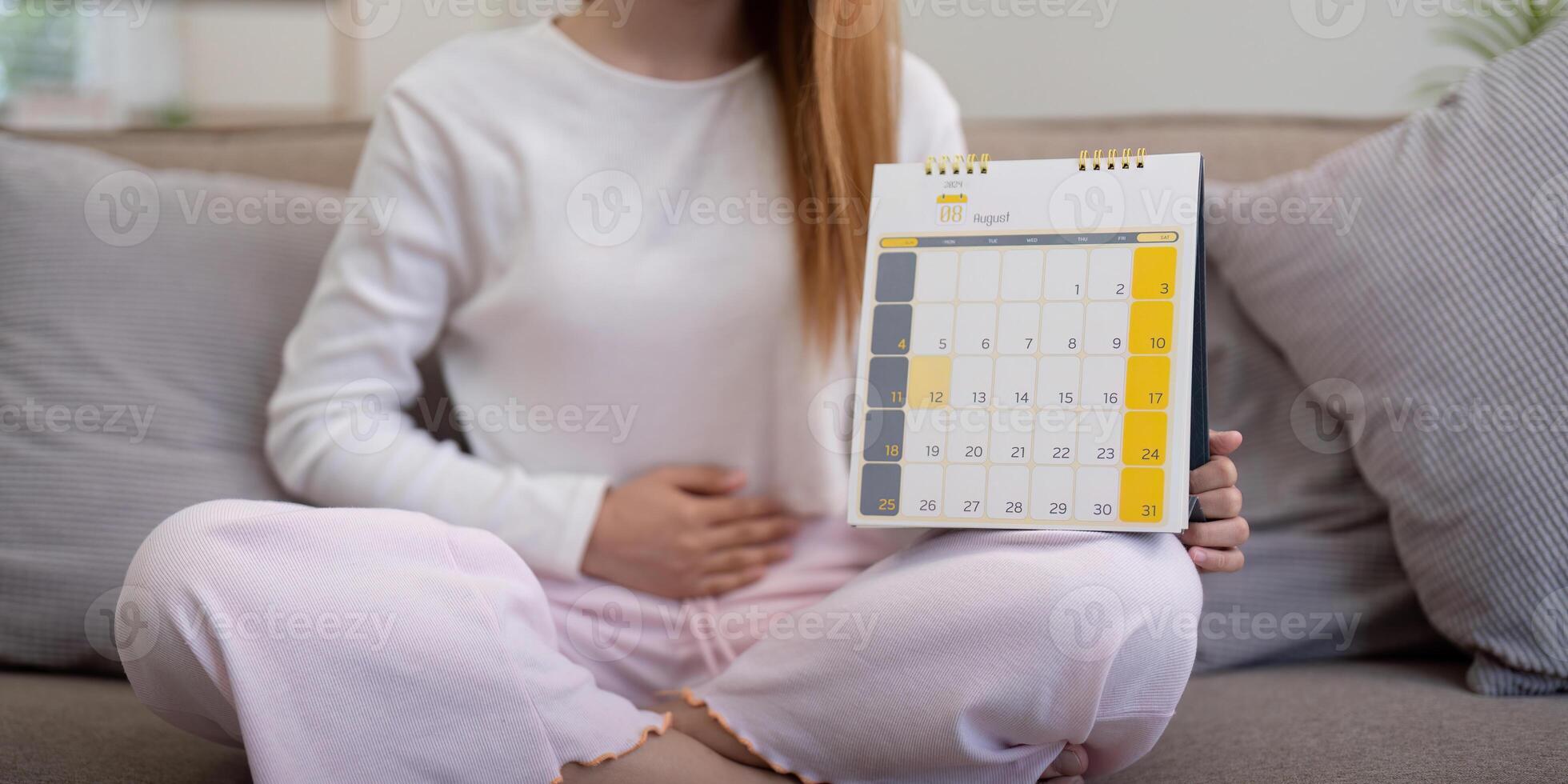 Woman sitting with a calendar and holding her stomach. Concept of menstrual cycle tracking and health photo