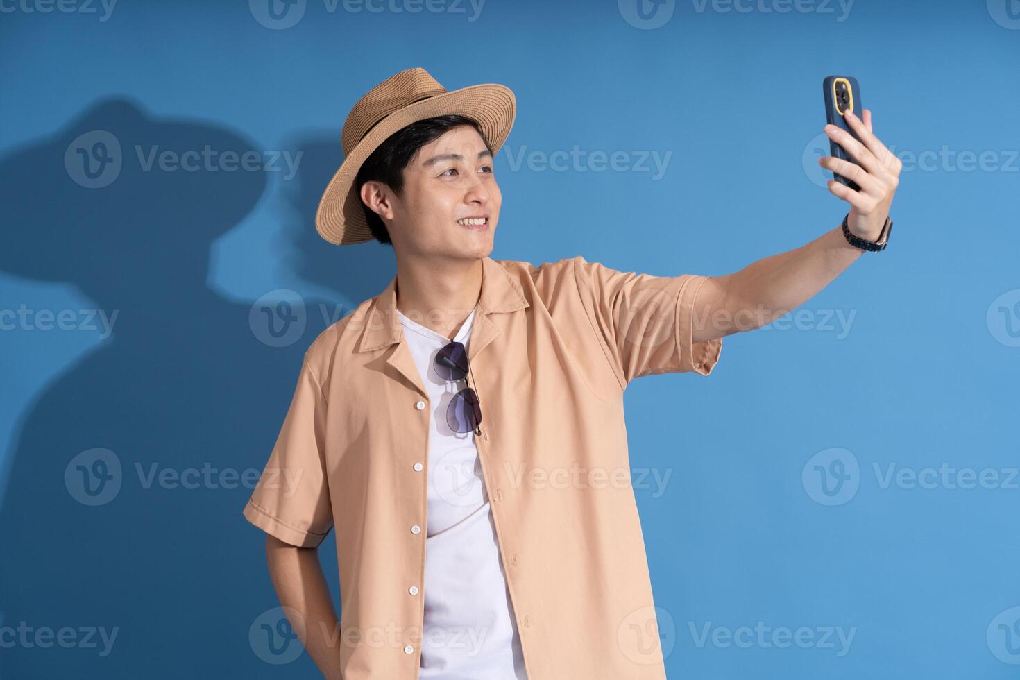 Portrait of Asian man posing on blue background, traveling in summer photo
