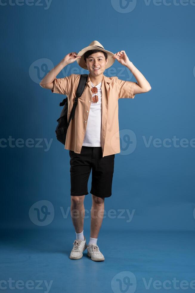 Portrait of Asian man posing on blue background, traveling in summer photo