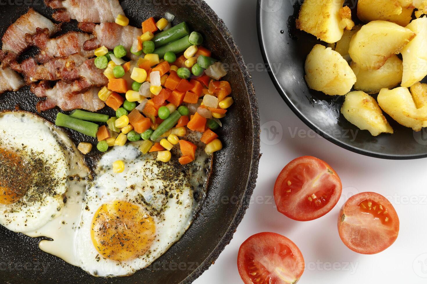 Fried eggs with vegetables, fried bacon and potatoes. Hearty food and a delicious lunch. photo