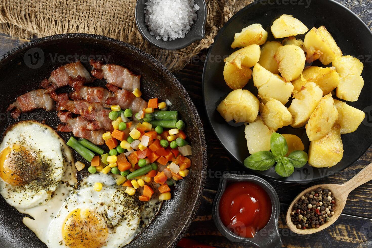 Fried eggs with vegetables, fried bacon and potatoes. Hearty food and a delicious lunch. photo
