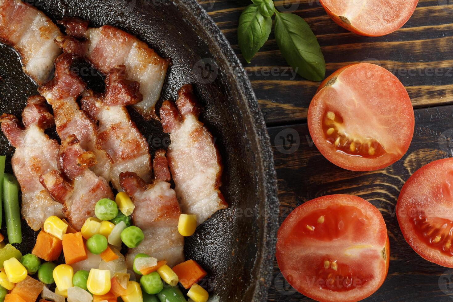 Fried bacon with vegetables and tomatoes in a pan. photo