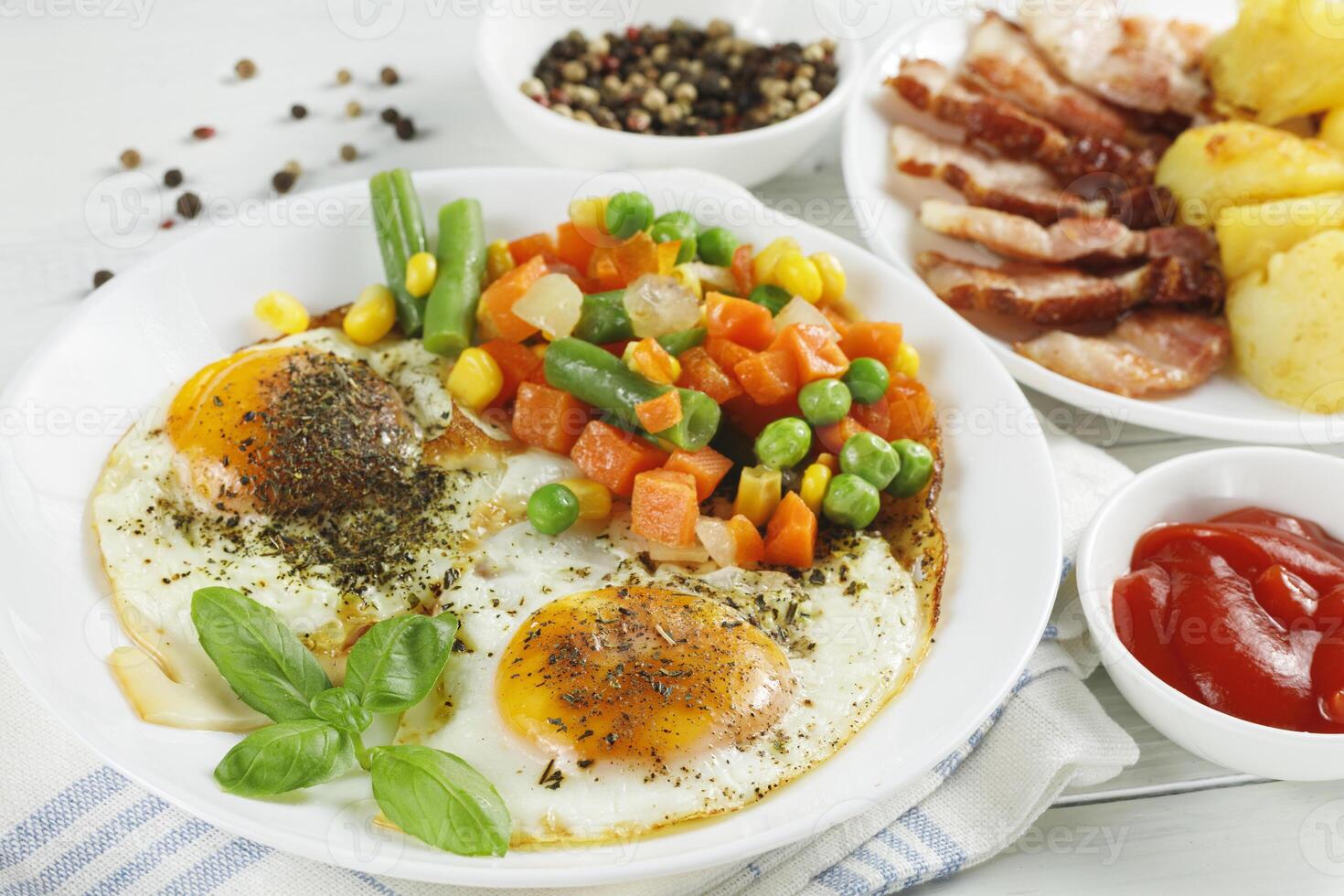 Fried eggs with vegetables, fried bacon and potatoes. Hearty food and a delicious lunch. photo