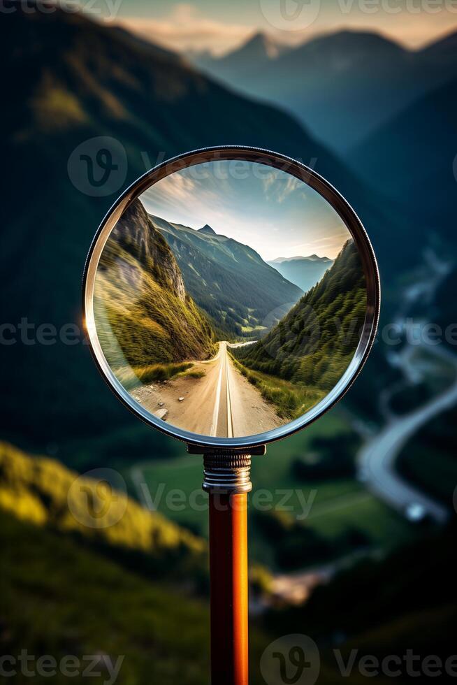close-up of a magnifying glass in which a beautiful mountain landscape and road are visible photo