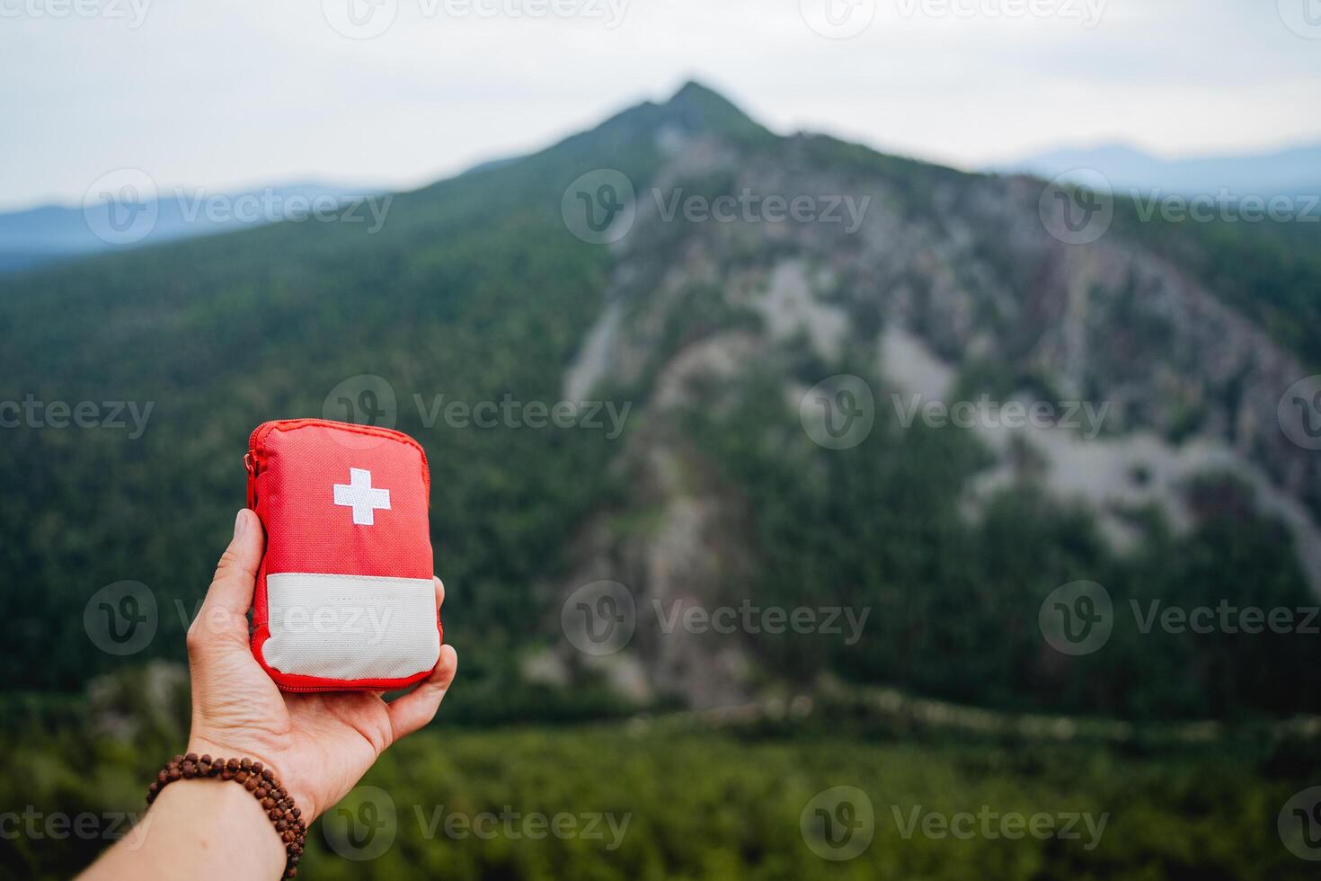 demonstration of a first aid kit on a hike, a hand holding a first aid kit, a red bag with medicines against the background of mountains, equipment on a hike. photo