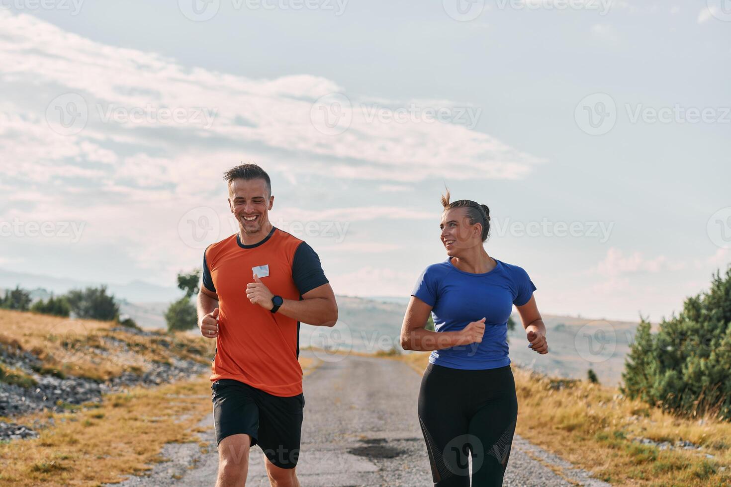 A couple dressed in sportswear runs along a scenic road during an early morning workout, enjoying the fresh air and maintaining a healthy lifestyle photo