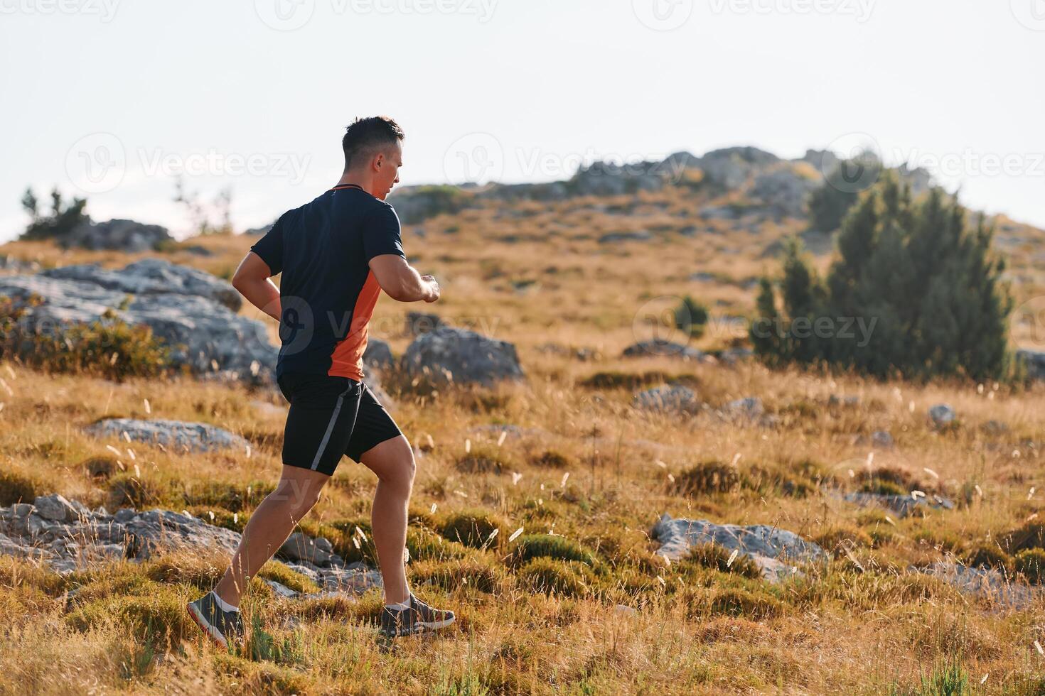 Determined Athlete Running Through Rugged Mountain Terrain at Sunrise. photo