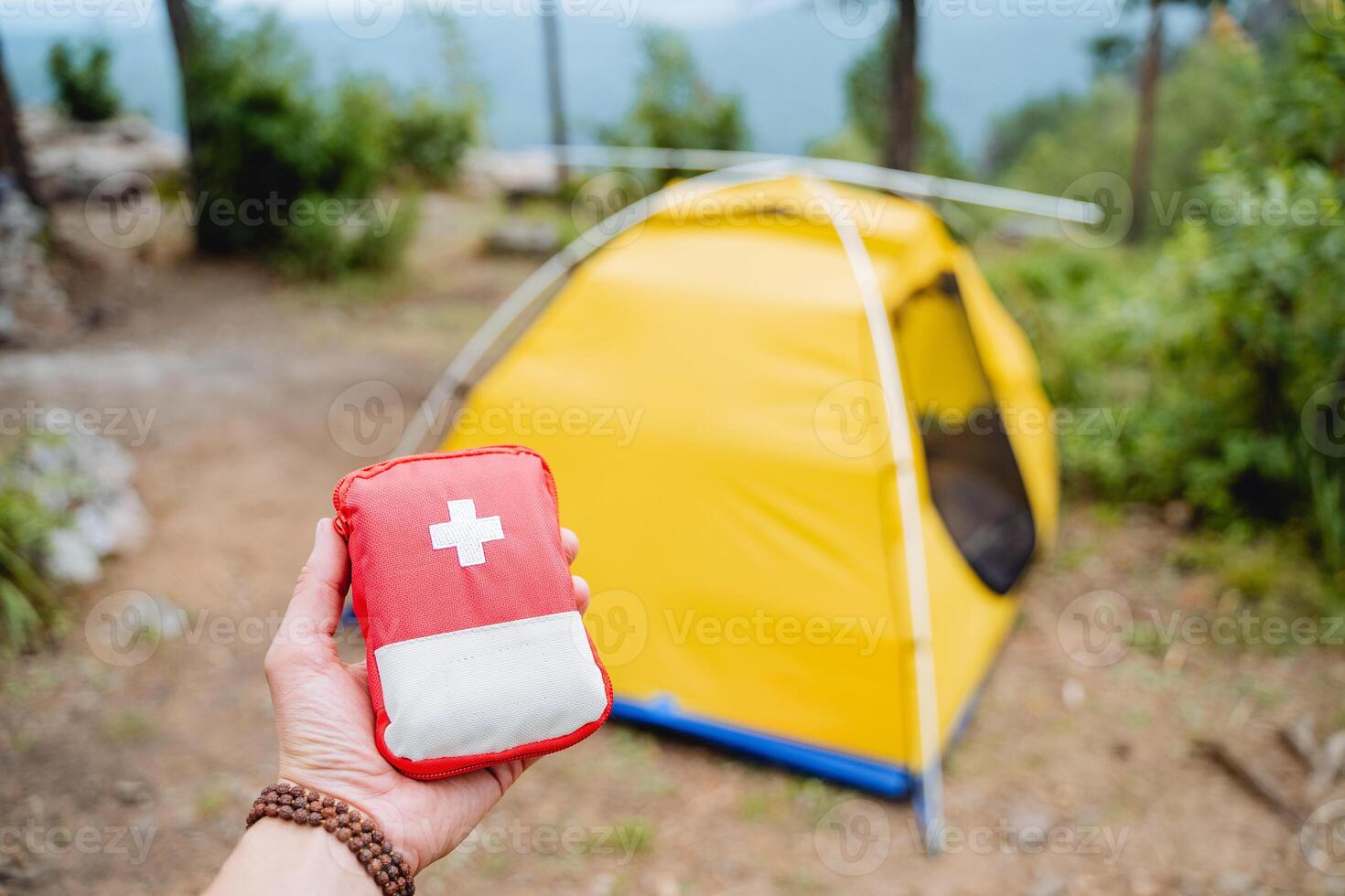 First aid kit in the mountains, extreme set of medicines, red first aid kit on the background of the tent, equipment on a hike, hand holding a minibag with medicines photo