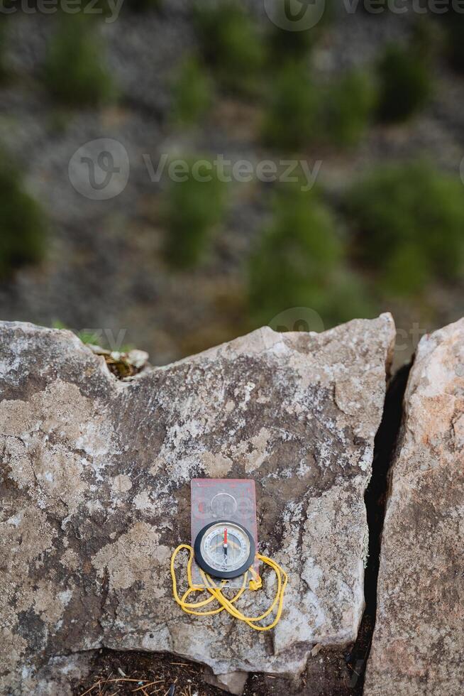 The compass lies on a rock. Sports tourist compass for orienteering on the ground. photo