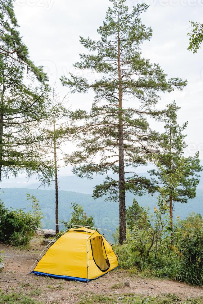 Yellow tourist tent stands in the mountains among pine trees, summer camping outdoor recreation, metal tent frame, arches photo