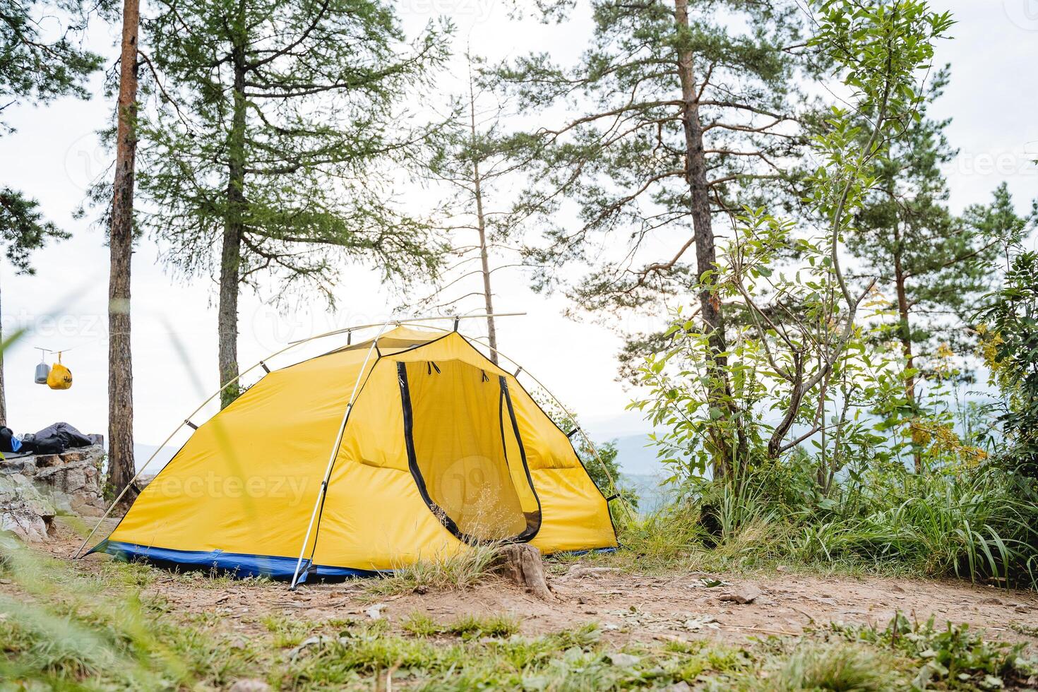 A yellow tent stands in the forest high in the mountains, tourist camping, a summer day in nature, a vacation in the forest, an open entrance. photo