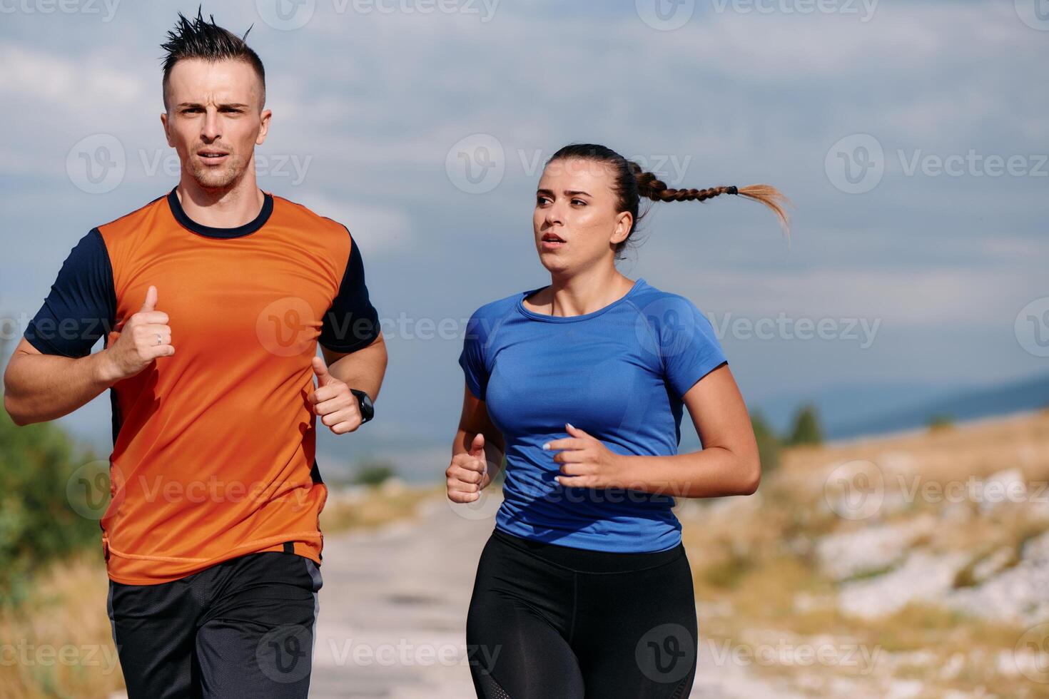 A couple dressed in sportswear runs along a scenic road during an early morning workout, enjoying the fresh air and maintaining a healthy lifestyle photo
