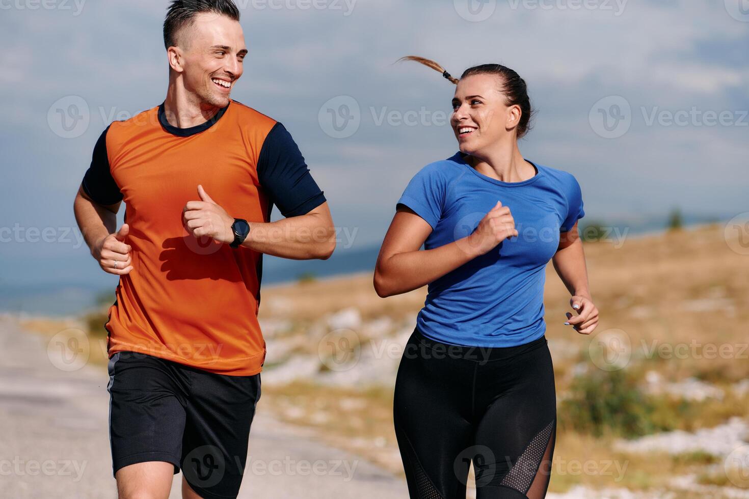A couple dressed in sportswear runs along a scenic road during an early morning workout, enjoying the fresh air and maintaining a healthy lifestyle photo