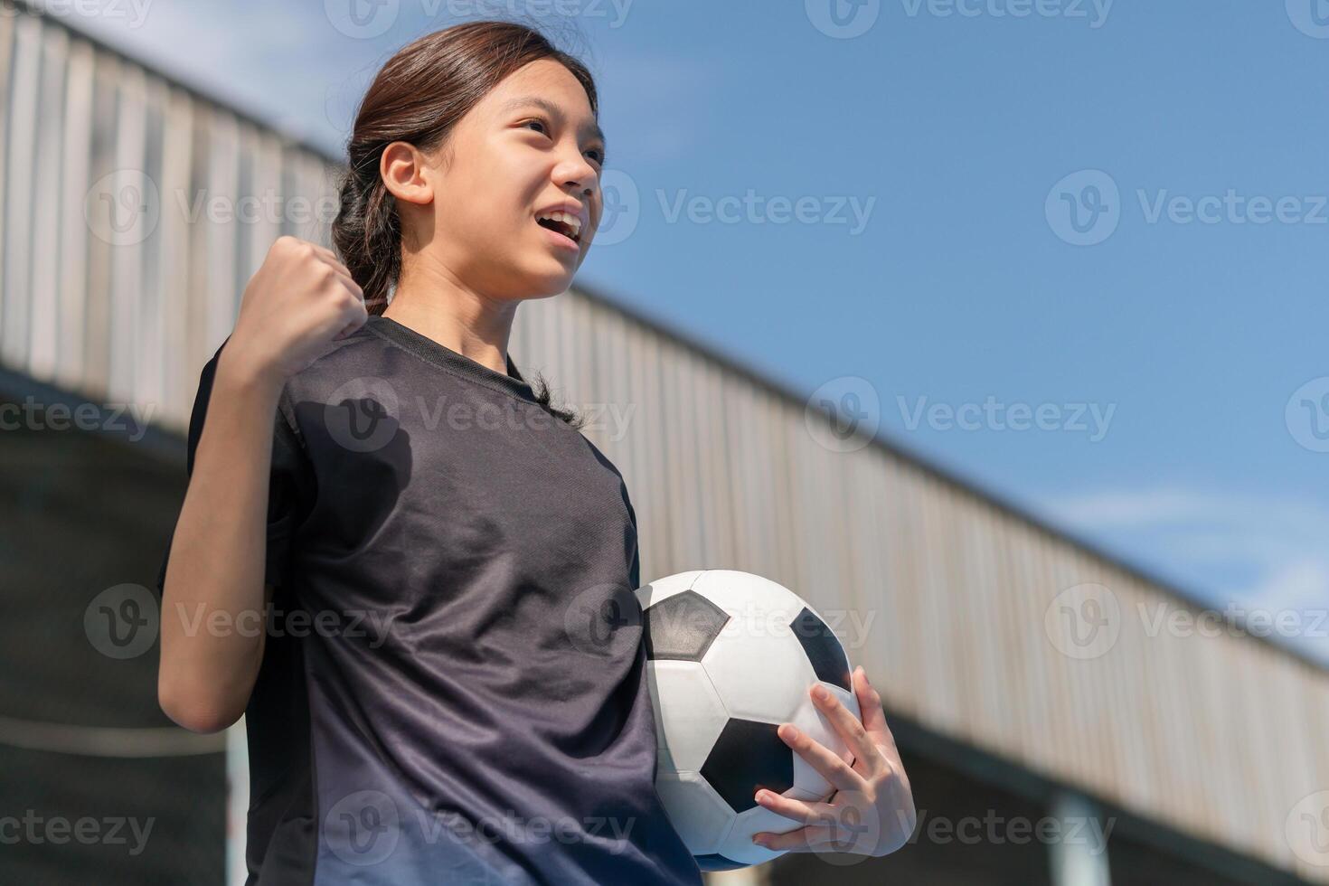 Excited Asian kid girl holding a football celebrates photo