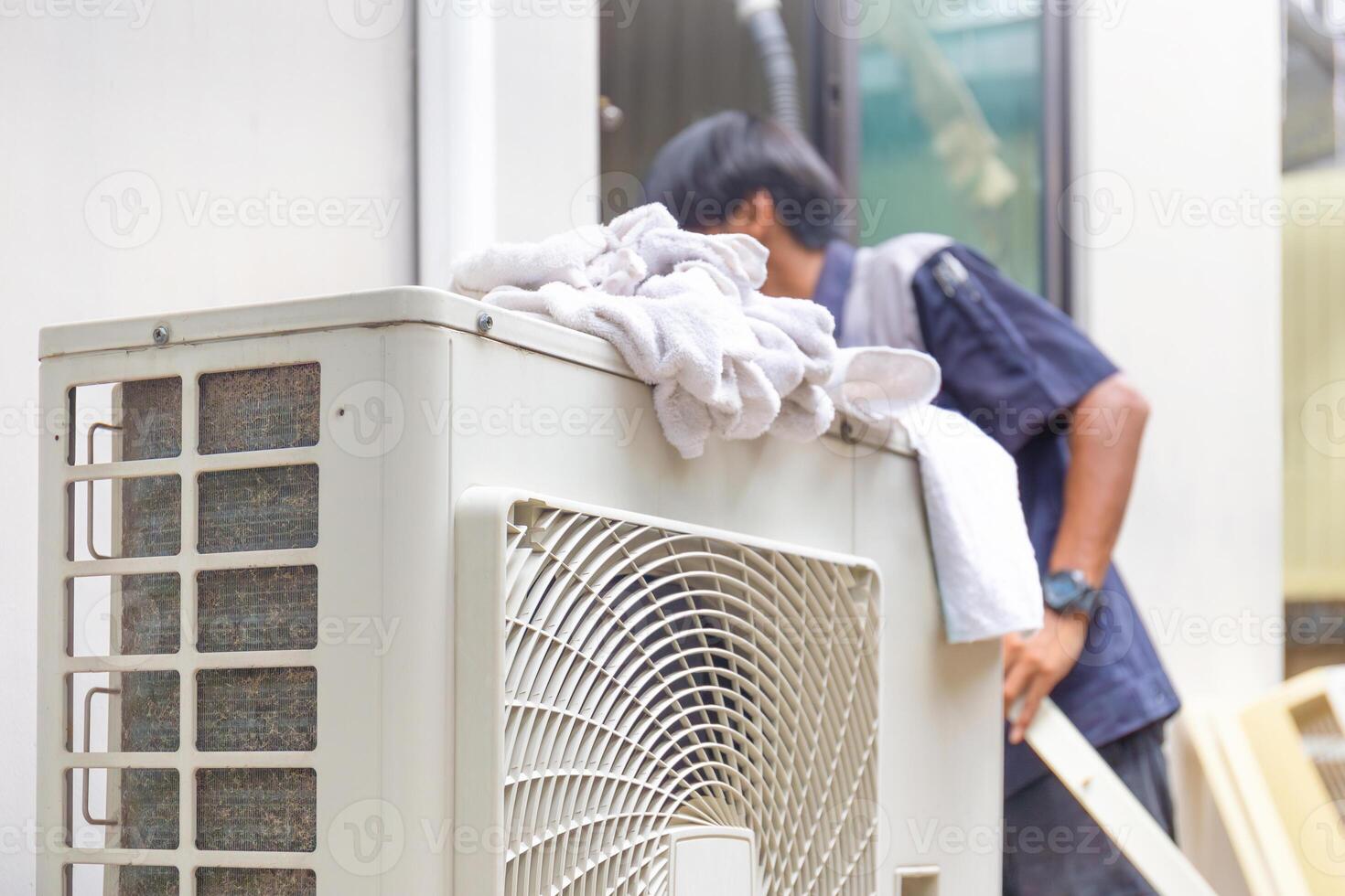 Selective focus of Air conditioner compressor with blurred technician man cleaning air conditioner in background, Repairman washing dirty compartments air conditioner photo