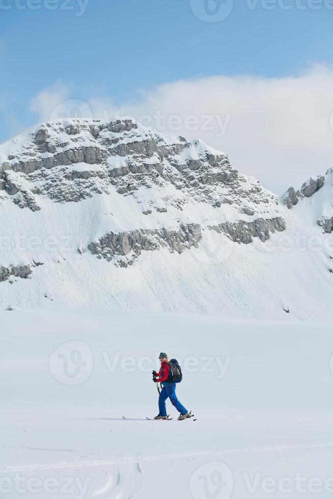 A female skier stands at the snowy summit of a mountain, equipped with professional gear and skis, poised for an exhilarating descent. photo