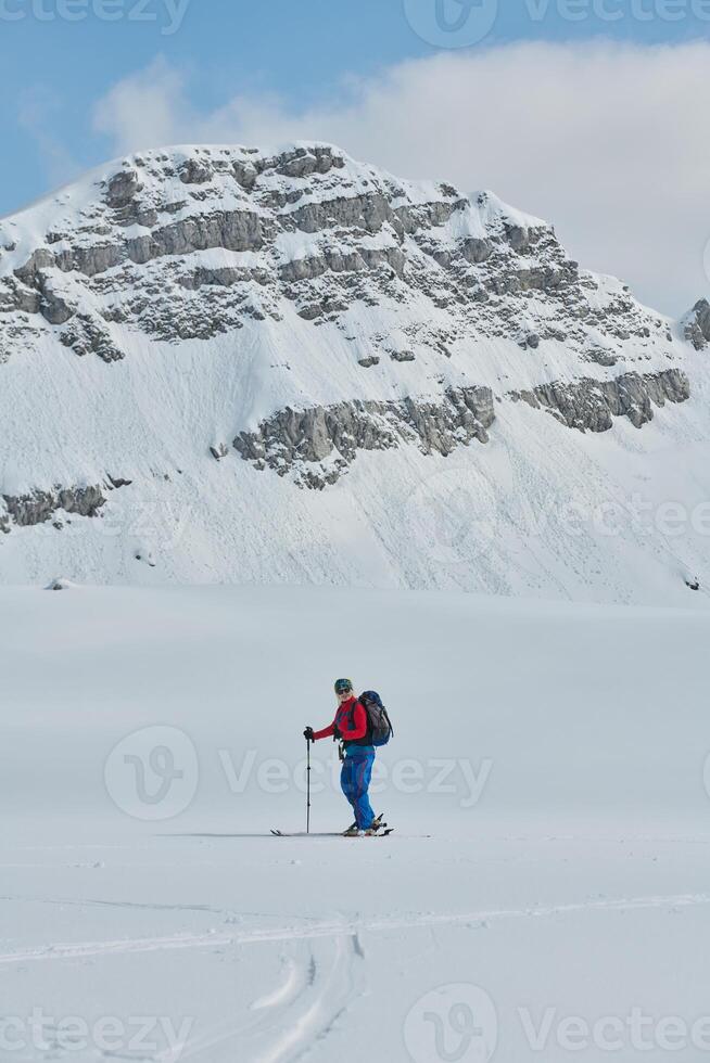 A female skier stands at the snowy summit of a mountain, equipped with professional gear and skis, poised for an exhilarating descent. photo